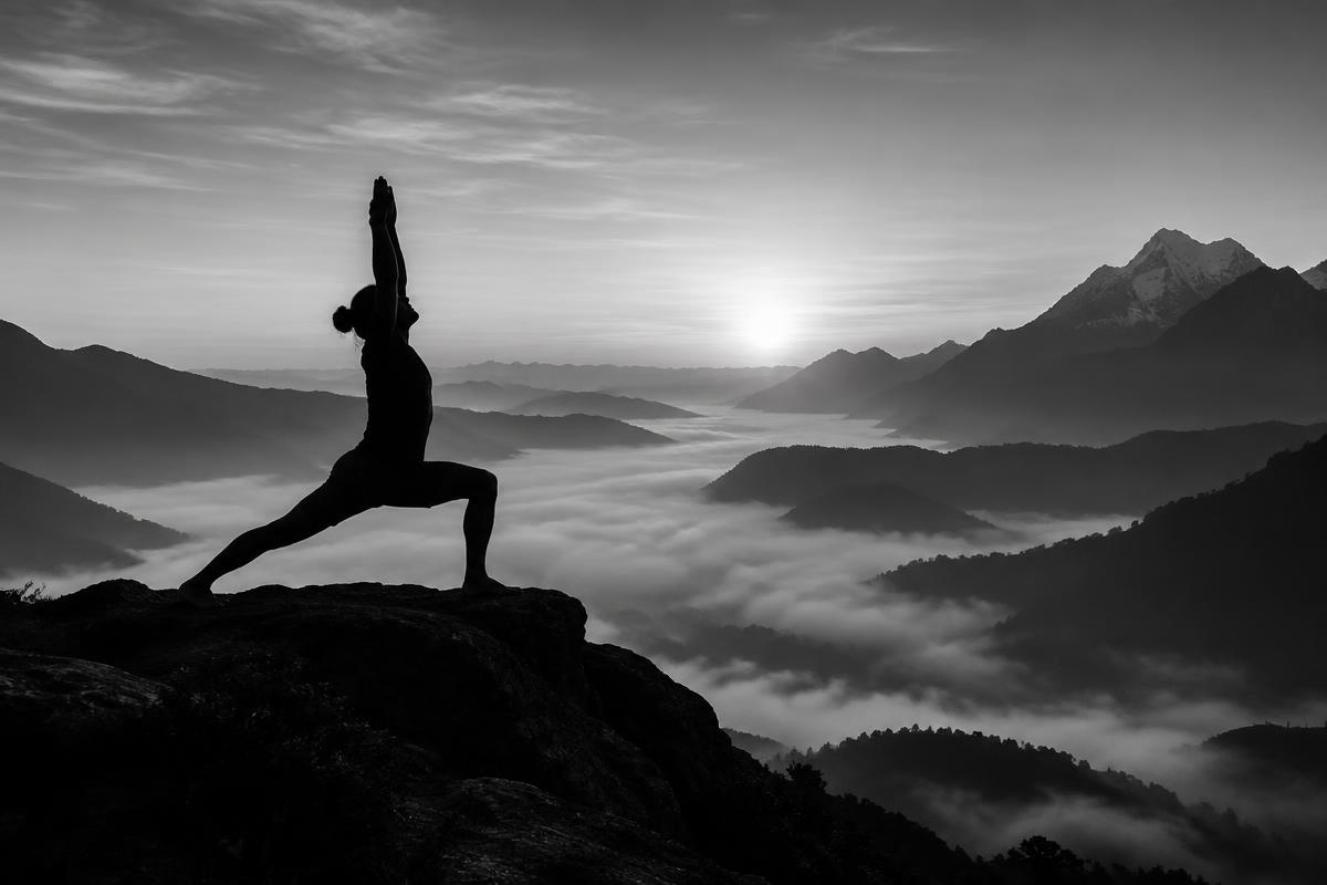 Silhouette of a yogi in warrior pose on a ridge above a sea of clouds, black and white