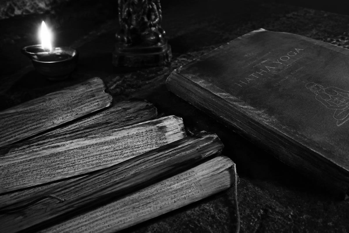 Palm-leaf manuscripts and an old Hatha Yoga book beside an oil flame, black and white