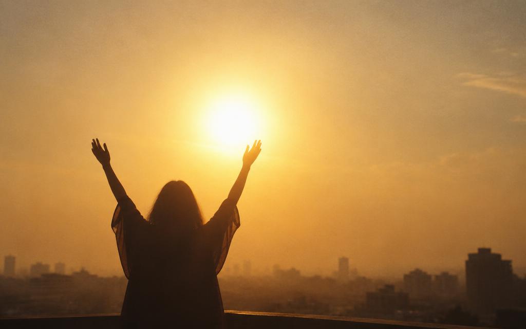 A silhouetted figure raising their arms to the rising sun